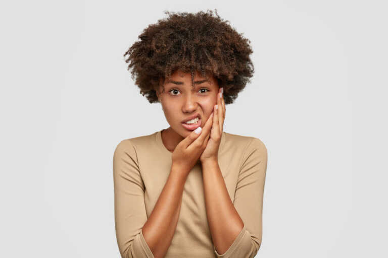 mulher negra tocando a bochecha com sensibilidade nos dentes