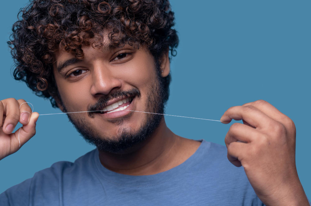 Homem utilizando fio dental nos dentes